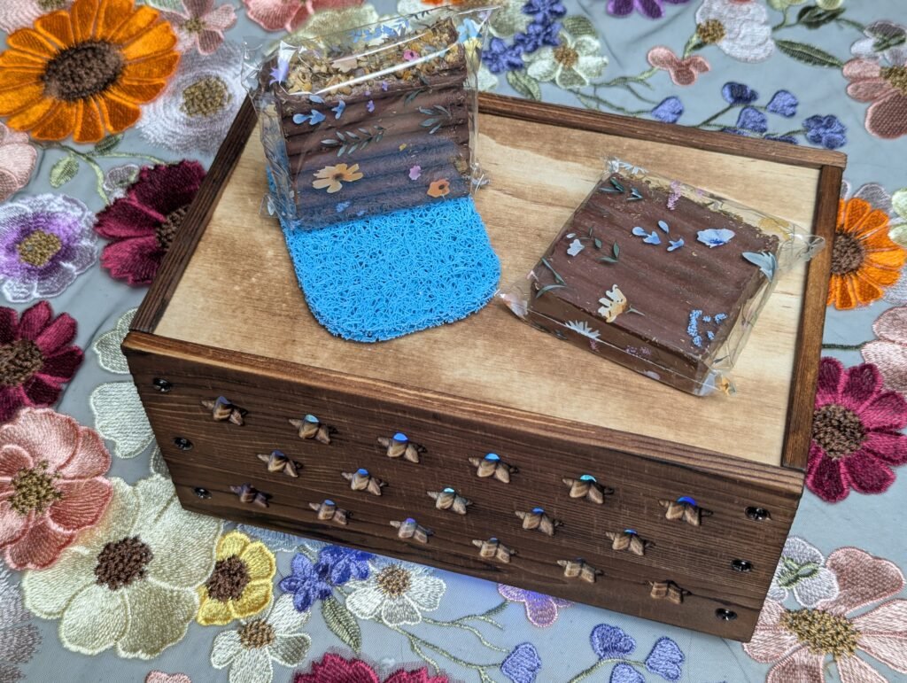 Two Uplifting Scented Artisan Bar Soaps in wrappers resting on blue soap scrubbing pad